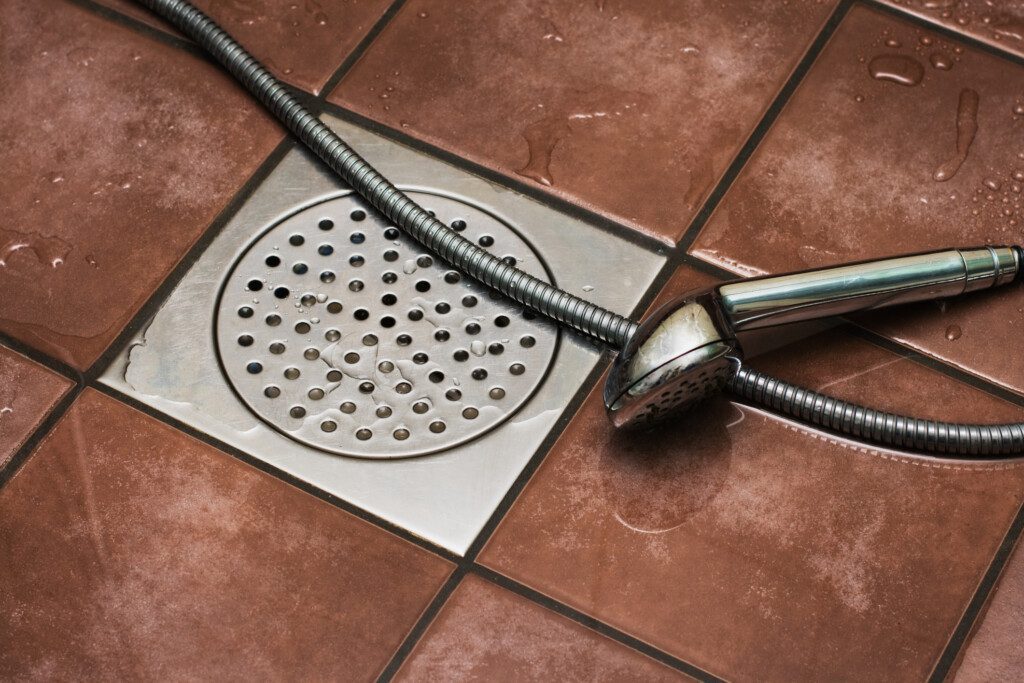 Imagem horizontal de uma ducha sobre um ralo de banheiro de inox
