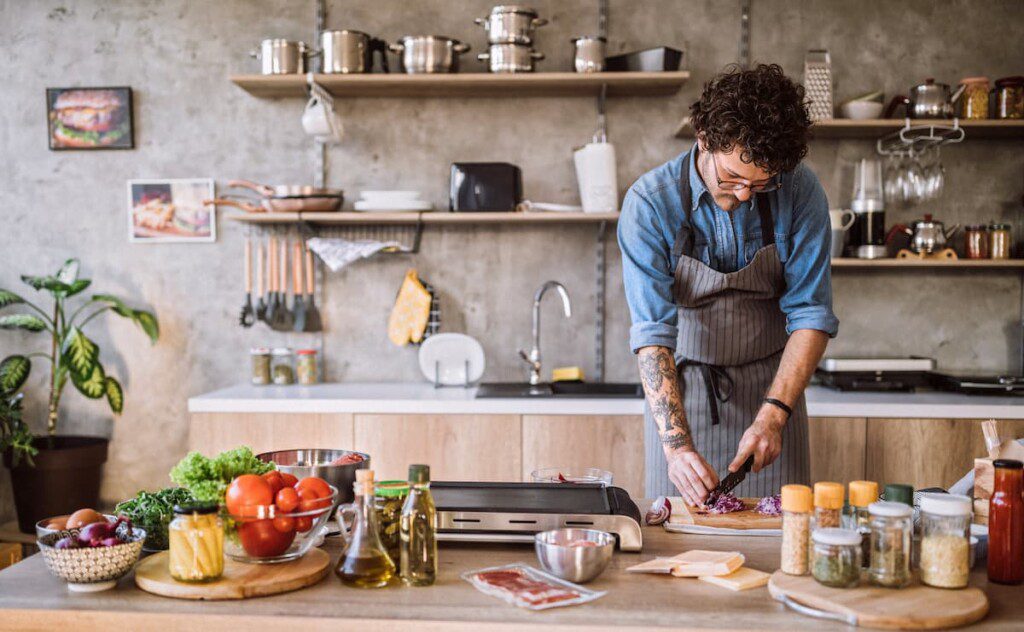 Homem prepara uma receita em uma cozinha com a parede com cimento queimado.