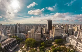 Imagem da vista aérea da praça Santos Andrade, no Centro de Curitiba, mostra vegetação e prédios ao redor em um dia de céu azul para ilustrar matéria sobre os melhores bairros de Curitiba
