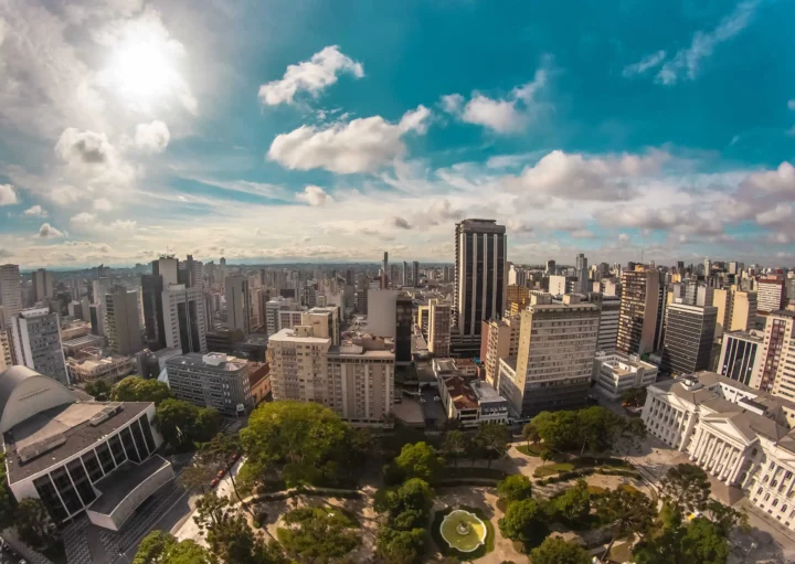 Imagem da vista aérea da praça Santos Andrade, no Centro de Curitiba, mostra vegetação e prédios ao redor em um dia de céu azul para ilustrar matéria sobre os melhores bairros de Curitiba