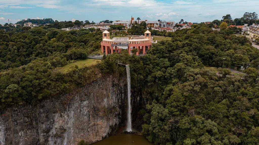 Imagem da vista aérea do Parque Tanguá, em Curitiba, mostra prédios, vegetação e cachoeira do local