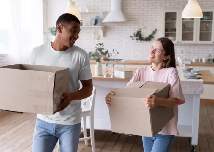 Imagem de um casal composto por um homem e uma mulher carregando caixas de papelão dentro de uma casa para ilustrar matéria sobre as cidades do interior de SP