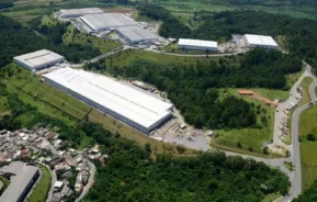 Imagem da vista aérea de um grande complexo industrial em Embu das Artes com vários galpões de telhado branco, cercado por vegetação e estradas, para ilustrar matéria sobre o que fazer em Embu das Artes