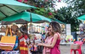 Imagem de duas molheres olhando produtos de artesanato em uma feira de rua para ilustrar matéria sobre as feiras em SP