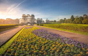 Imagem panorâmica do jardim ao redor da estufa do Jardim Botânico de Curitiba durante o nascer do sol