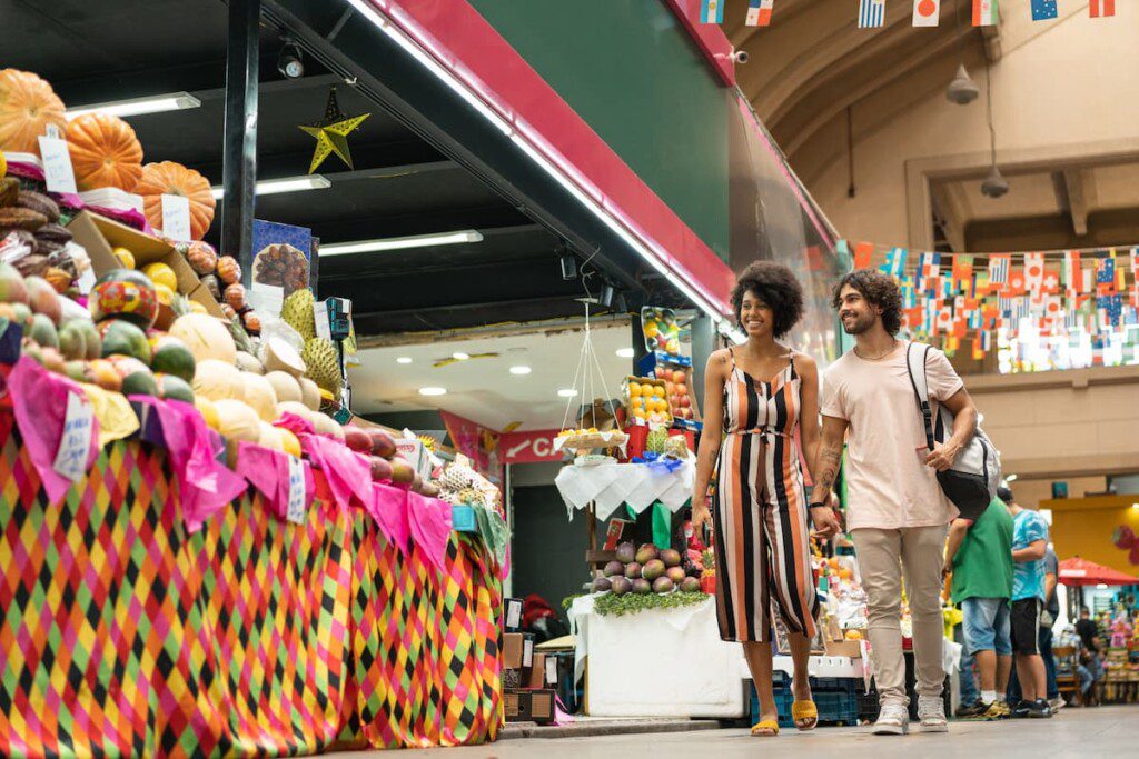 Casal passa por uma banca de frutas no interior do Mercado Municipal de São Paulo.