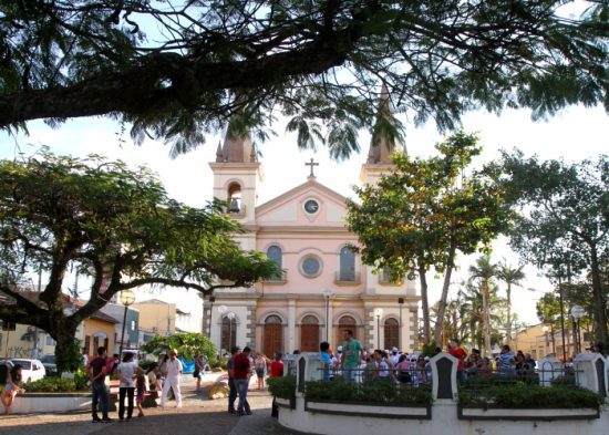 Pessoas transitam em uma praça de uma igreja.