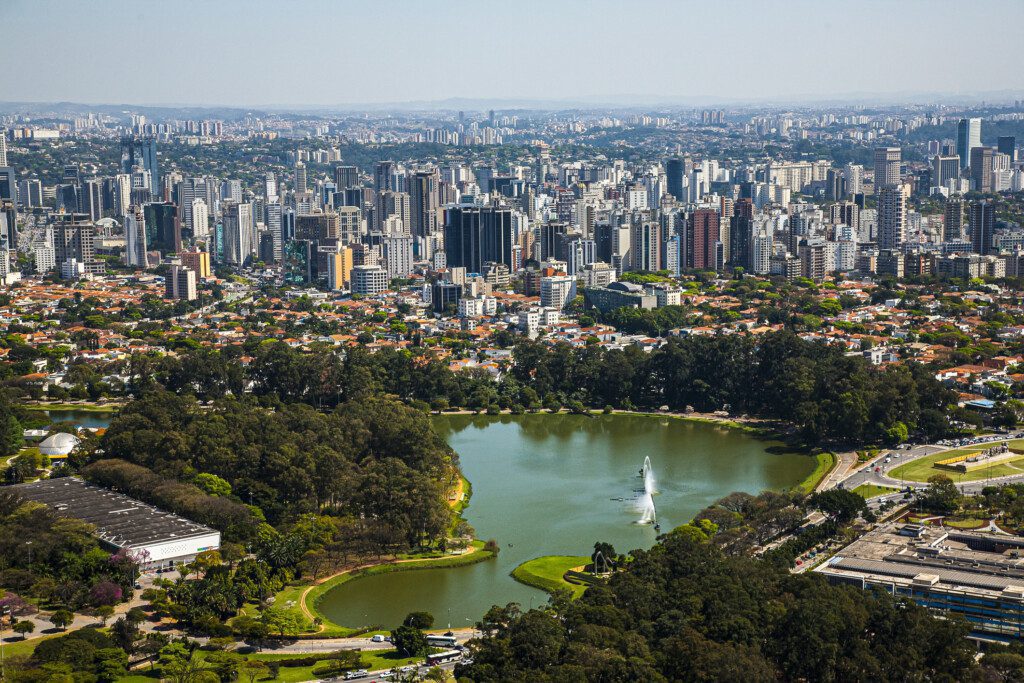 Imagem aérea da paisagem do Parque Ibirapuera, em São Paulo, mostra prédios altos, árvores e um lago