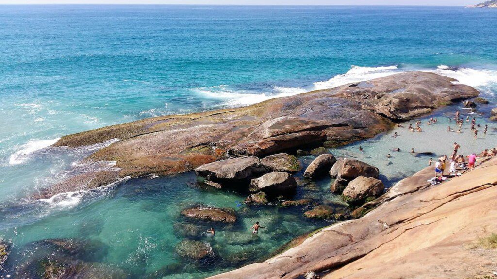 Pessoas se divertindo em uma piscina natural no meio de uma rocha à beira mar.