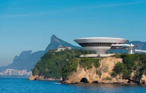 Foto mostra o Museu de Arte Contemporânea de Niterói, com o morro do Corcovado ao fundo (Crédito: WikiCommons)