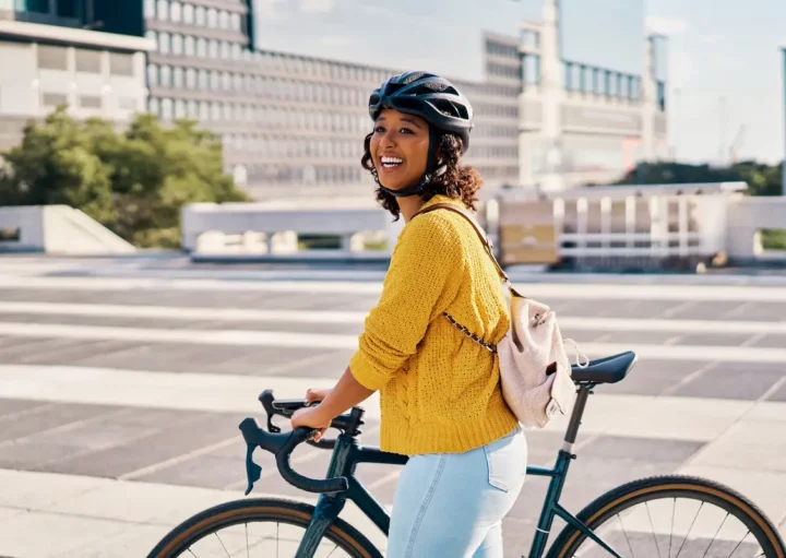 Uma mulher caminha, em uma cidade, ao lado de sua bicicleta.