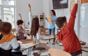 Imagem de uma sala de aula com alunos de costas sentados em carteiras em frente a uma professora para ilustrar matéria sobre as melhores escolas da Zona Oeste de SP