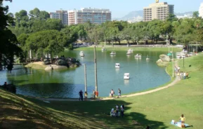 Imagem panorâmica de parte do parque, com vista para o lago com pedalinhos e visitantes fazendo piquenique para ilustrar matéria sobre a Quinta da Boa Vista Rio de Janeiro, RJ