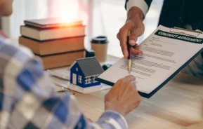 Imagem de um homem entregando uma prancheta com documento e uma caneta para outro homem vestido de azul para ilustrar matéria sobre declaração de residência para inquilino