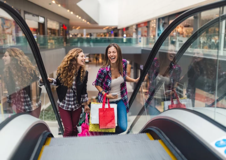 Imagem de duas mulheres jovens segurando sacolas em uma escada rolante de um shopping para ilustrar matéria sobre shopping em bh