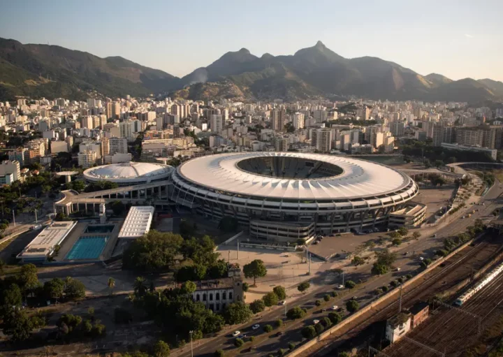 Foto que ilustra matéria sobre o estádio do Maracanã mostra o complexo onde fica a arena vista do alto, com prédios e montanhas do Rio de Janeiro ao fundo.