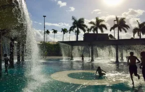 Foto que ilustra matéria sobre o Parque Madureira mostra crianças brincando em uma fonte artificial de águas ao cair do sol