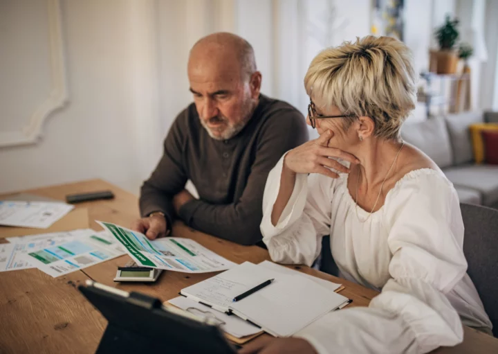 imagem que ilustra matéria sobre IOF financiamento imobiliario mostra um casal sentado em frente à uma mesa cheia de papeis