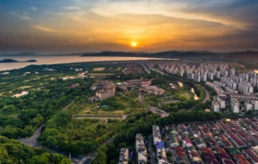 Imagem aérea do por do sol de uma região bem dividida: de um lado, casas residenciais e, outro, vasta floresta com árvores verdes para ilustrar matéria sobre bairro residencial