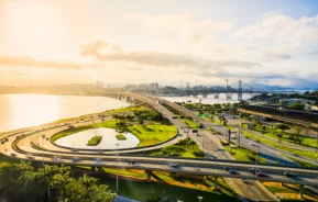 Imagem aérea de carros nos viadutos e pistas próximos ao mar durante o nascer do sol em Florianópolis para ilustrar matéria sobre cidades tranquilas para morar