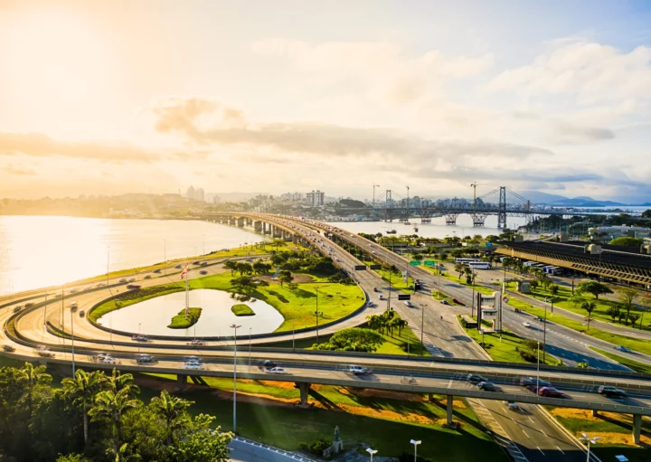 Imagem aérea de carros nos viadutos e pistas próximos ao mar durante o nascer do sol em Florianópolis para ilustrar matéria sobre cidades tranquilas para morar