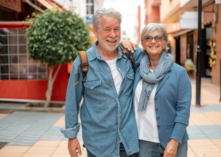 Imagem de um casal de idosos composto por um homem e uma mulher brancos, de cabelos brancos, sorridentes e vestindo camisetas jeans para ilustrar matéria sobre cidade para idosos no Brasil