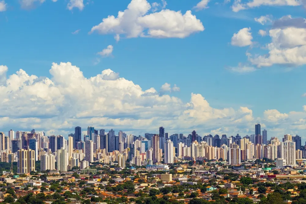 Imagem da vista aérea de Goiânia, capital do estado de Goiás, mostra prédios do município, casas e vegetação em um dia de céu azul