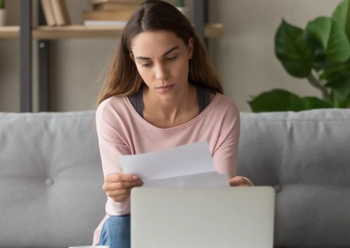 Foto que ilustra matéria sobre cota condominial mostra uma jovem mulher segurando e olhando para um papel com um semblante preocupado (Foto: Shutterstock)