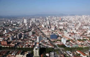 Imagem da vista aérea de Santos mostra casa, prédios, avenidas, vegetação e céu azul ao fundo para ilustrar matéria sobre os bairros nobres de Santos.