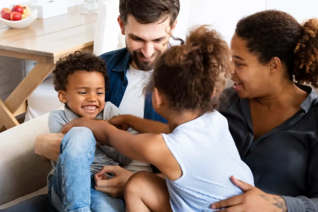 Imagem de uma família formada por um homem, uma mulher e duas crianças sorrindo enquanto se divertem juntos para ilustrar matéria sobre consórcio de imóvel: vale a pena?