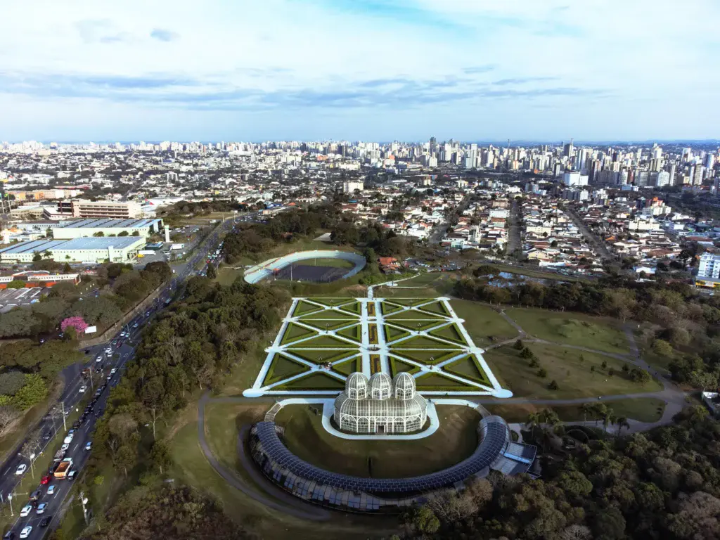 Imagem da vista aérea do Jardim Botânico de Curitiba mostra avenidas, vegetação e prédios da cidade ao fundo para ilustrar matéria sobre quais as melhores capitais do Brasil