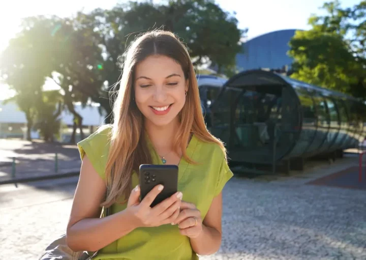 Foto que ilustra matéria sobre Cidades inteligentes no Brasil mostra uma mulher sorrindo enquanto olha para um celular próxima a uma estação de ônibus de Curitiba (Foto: Shutterstock)