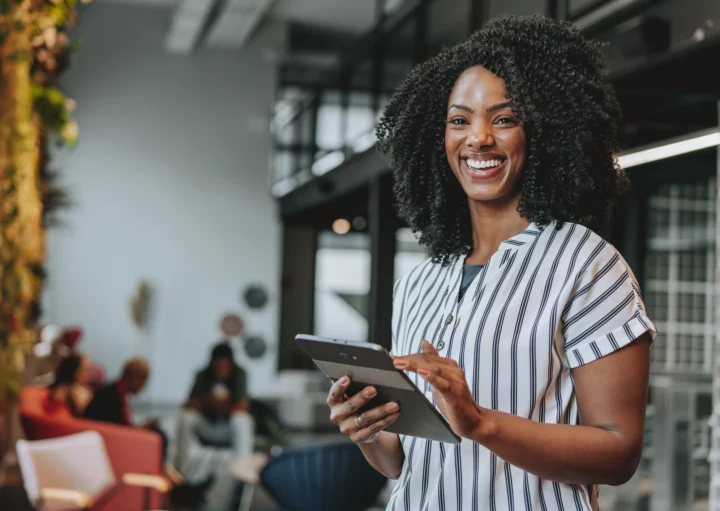 Mulher negra em ambiente empresarial sorrindo e segurando um tablet para ilustrar matéria sobre as cidades com mais empregos no Brasil