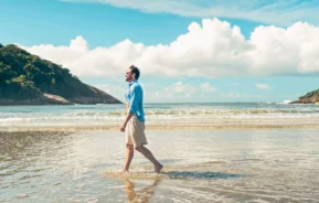 Imagem de um homem andando na faixa de areia de uma praia para ilustrar matéria sobre as cidades mais seguras do litoral de SP