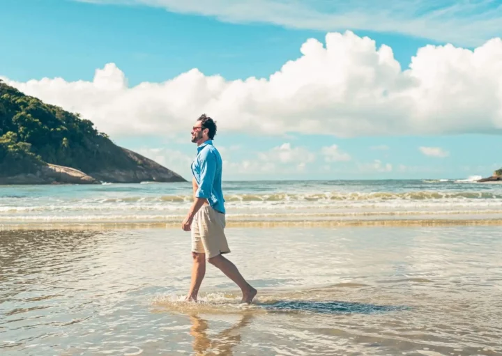 Imagem de um homem andando na faixa de areia de uma praia para ilustrar matéria sobre as cidades mais seguras do litoral de SP