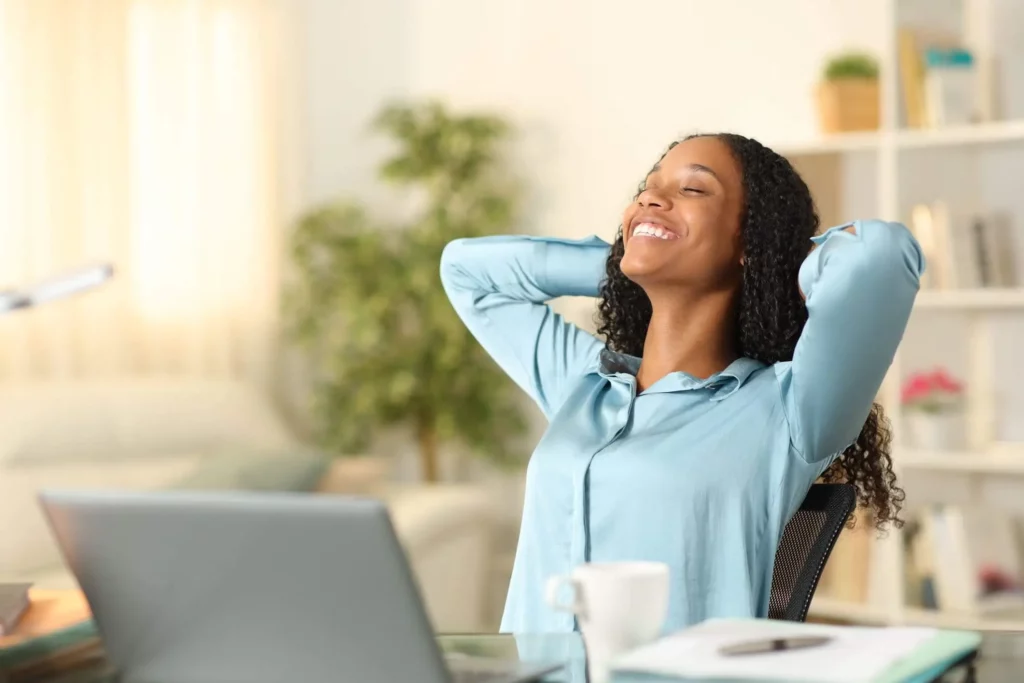 Imagem de uma mulher sorridente inclinada para trás no encosto da cadeira para ilustrar matéria sobre as vantagens de investir em imóveis e adquirir renda passiva