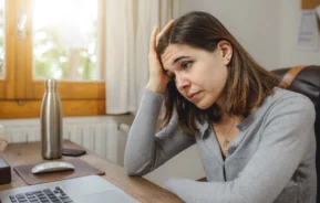 Imagem que ilustra matéria sobre se é possível alugar imóvel com nome sujo mostra mulher sentada em frente ao computador com uma cara de preoucupada