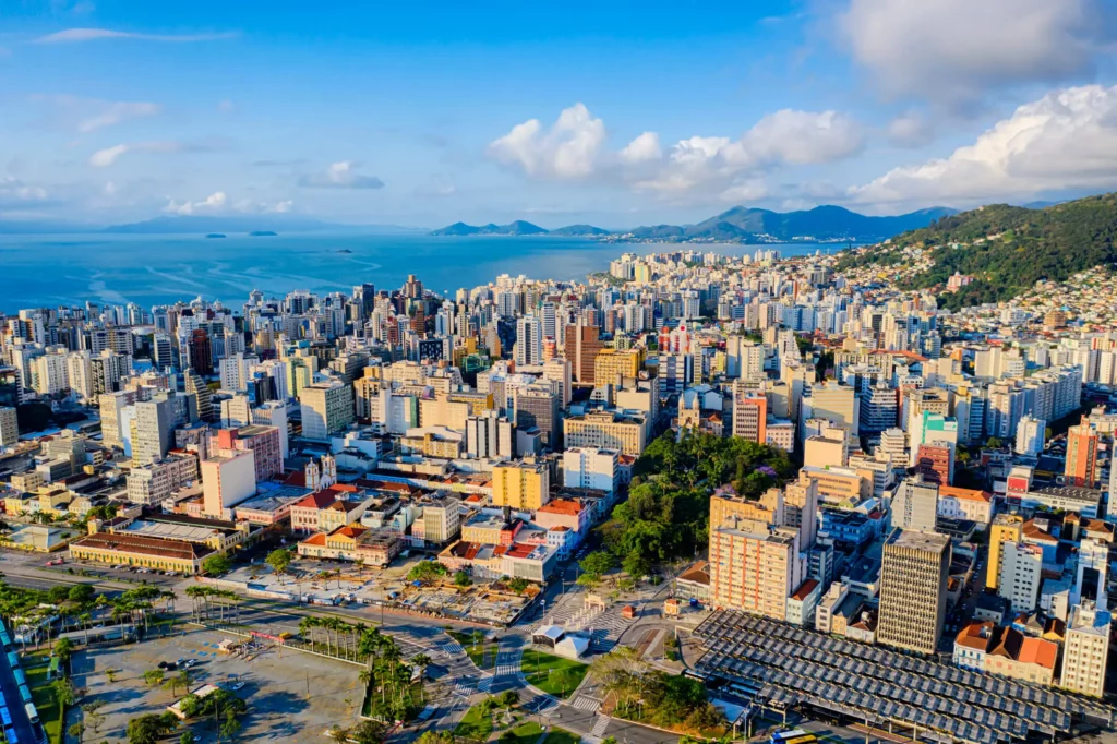 Imagem aérea de Florianópolis com vista para o mar e para região urbana com prédios para ilustrar matéria sobre cidades do litoral de Santa Catarina