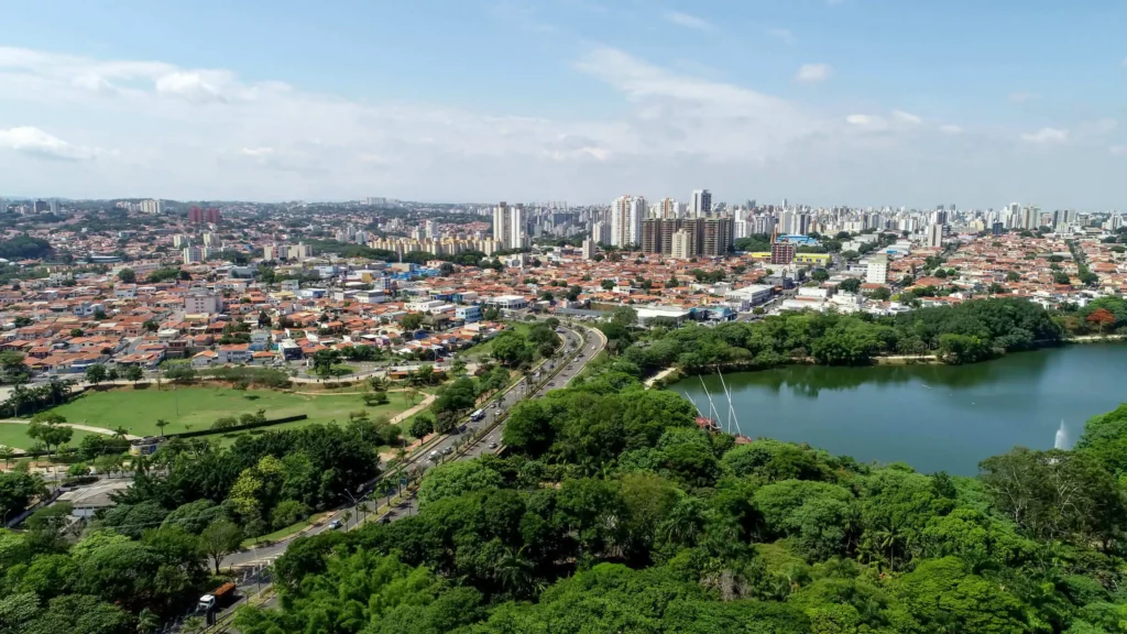 Imagem da vista aérea da cidade de Campinas mostra Lagoa do Taquaral, vegetação e prédios ao fundo