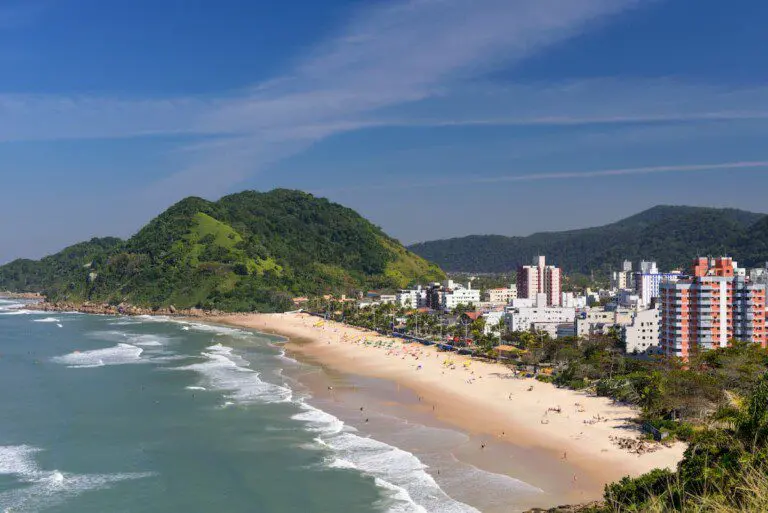 Imagem da vista aérea da Praia do Tombo, no Guarujá, mostra mar, faixa de areia, vegetação e prédios à beira-mar para ilustrar matéria sobre as melhores praias de SP para crianças