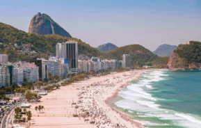 Imagem da praia de Copacabana mostra mar, faixa de areia, prédios e vegetação para ilustrar matéria sobre o que fazer na zona sul do Rio de Janeiro