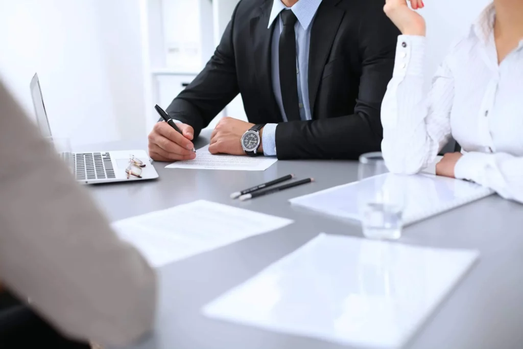 Imagem de um grupo de três pessoas sentadas ao redor de uma mesa com papéis, canetas e computador em cima para ilustrar a matéria sobre passo a passo para transferir iptu de falecido