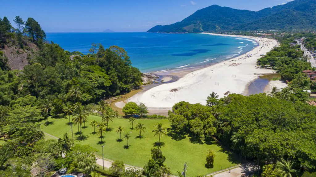 Imagem panorâmica da Praia de Maresias, em São Sebastião, mostra larga faixa de areia cercada por vegetação para ilustrar matéria sobre praias de São Paulo baratas