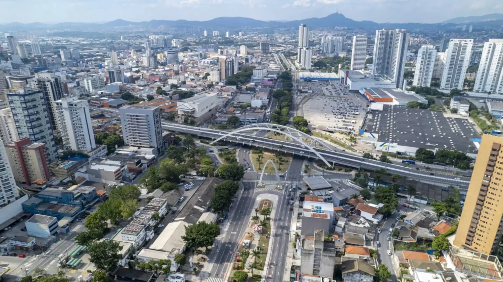 Imagem da vista aérea de Osasco mostra a Ponte Metálica, Viaduto reinaldo de Oliveira, avenidas, prédios, montanhas ao fundo e vegetação do município