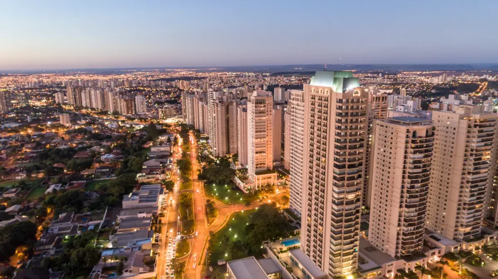Fotografia aérea da cidade de Ribeirão Preto mostra prédios, avenidas e vegetação da cidade no fim da tarde