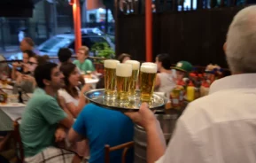 Foto que ilustra matéria sobre melhor vida noturna no Brasil mostra um garçom de costas com uma bandeja com copos cheios de chope nas mãos (Foto: Alexandre Macieira | Riotur)