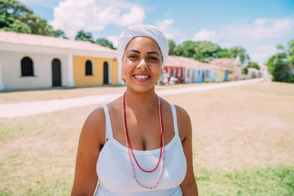 Imagem de uma mulher usando tradicional traje baiano na frente de construções coloridas para ilustrar matéria sobre o bairro mais populoso de Salvador