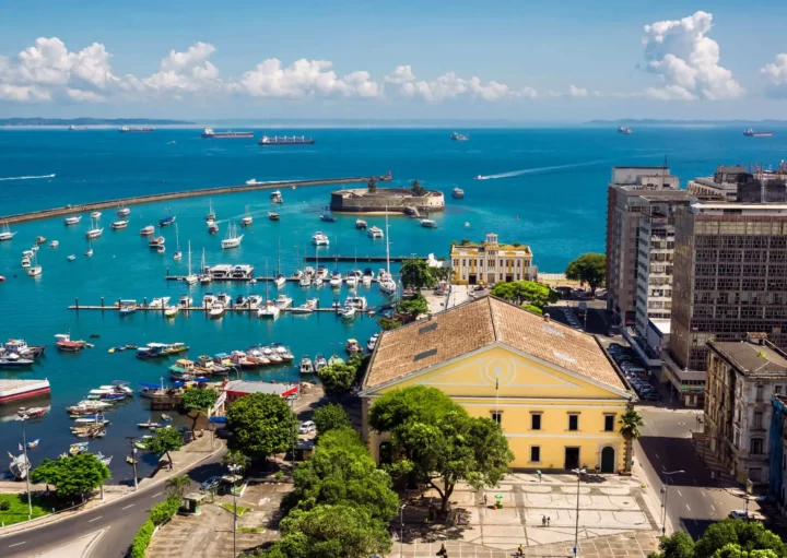 Imagem da vista aérea da Baía de Todos os Santos mostra mar, embarcações, vegetação e prédios para ilustrar matéria sobre os bairros mais populosos de Salvador