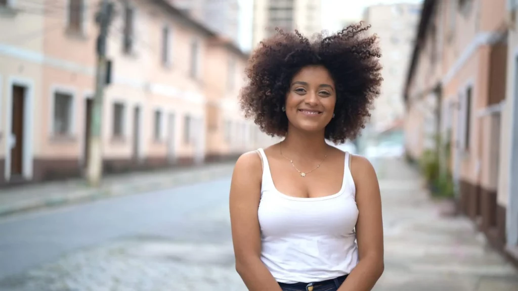 Imagem de uma mulher negra para no meio de uma rua que conta com prédios de arquitetura histórica para ilustrar matéria sobre como é morar na Zona Oeste de BH