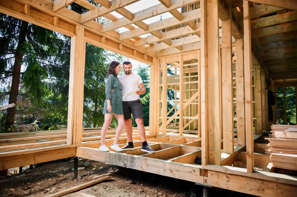 Imagem de um casal composto por um homem e uma mulher inspecionando sua futura casa de madeira em construção para ilustrar matéria que fala sobre construindo ou reformando